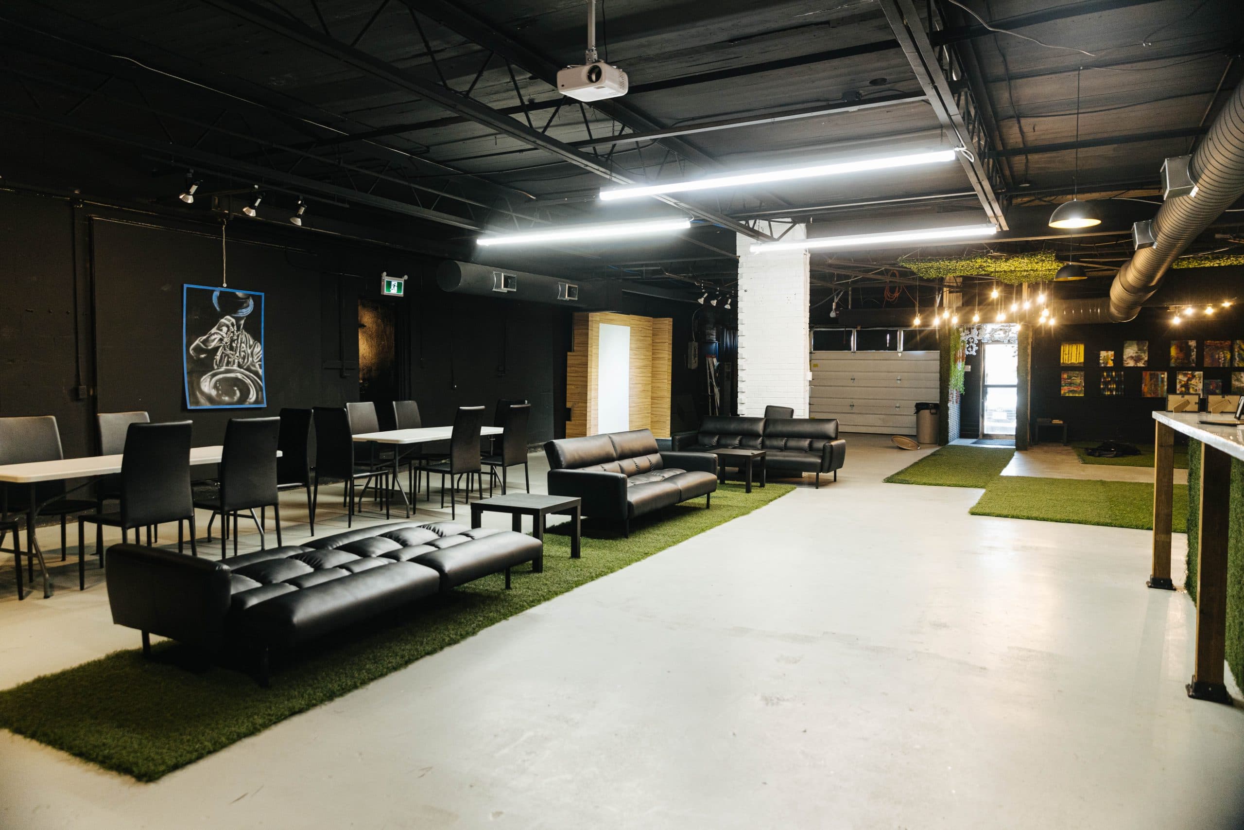 A long view down the room at Half Note past lounge seating and tables to the garage door, with an art wall and string lights at the far end.